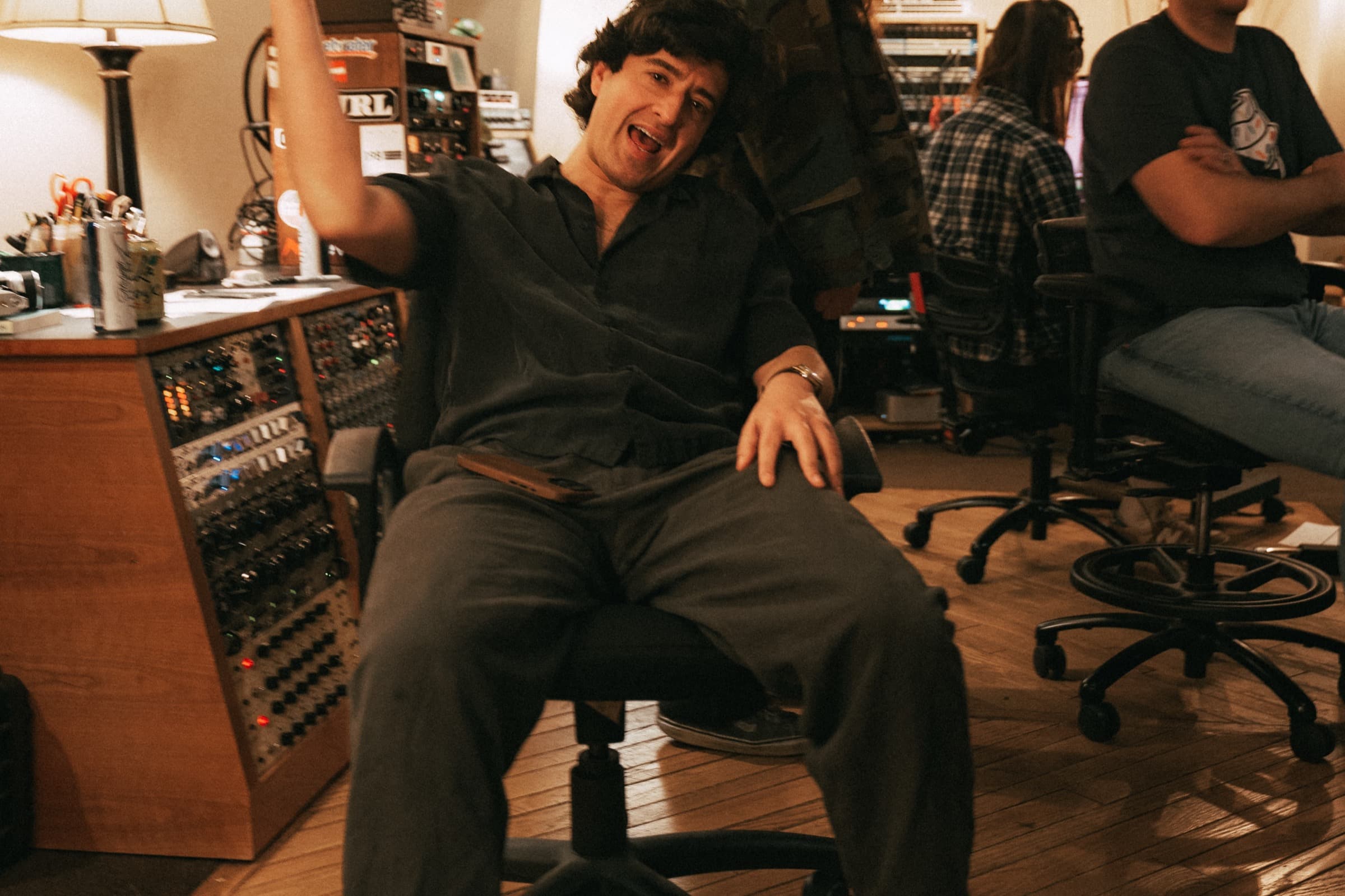 Joey Myron laughing in a chair beside a studio console