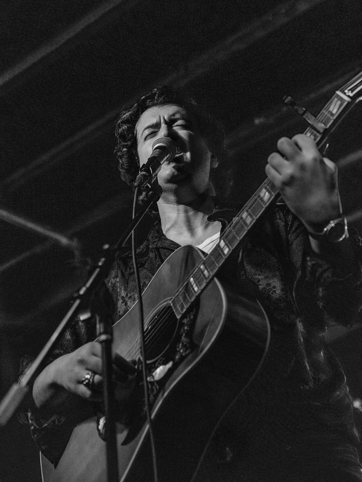 Joey Myron singing into the microphone with an acoustic guitar