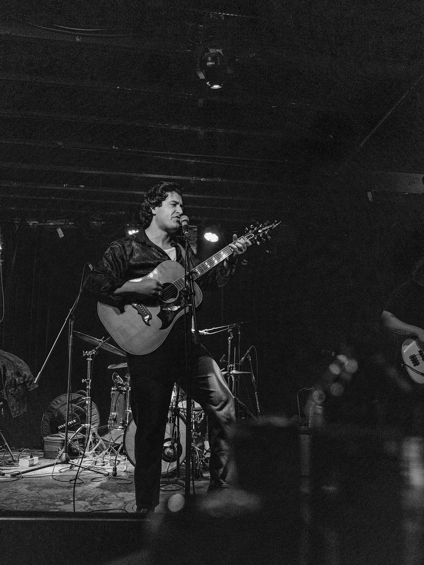 Joey Myron on a dark stage with an acoustic guitar